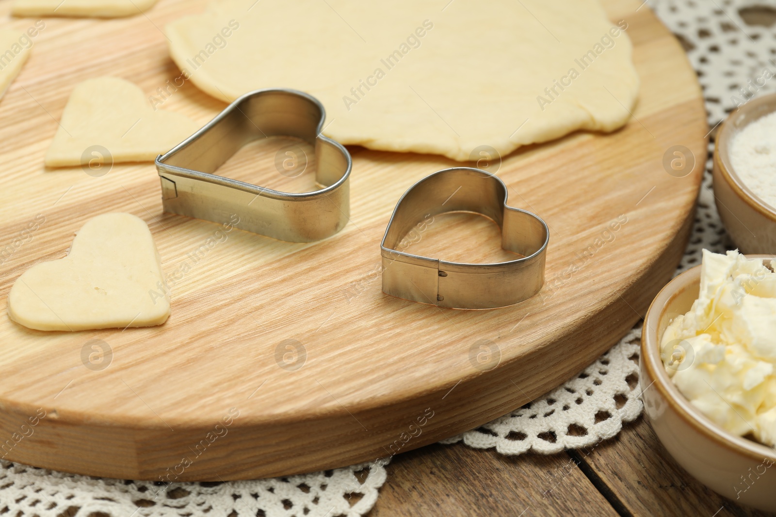 Photo of Raw dough and cookie cutters on wooden table, closeup