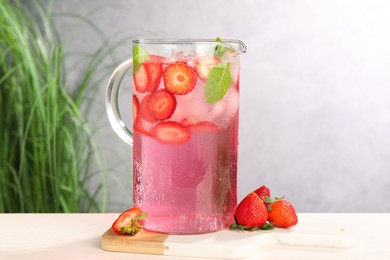 Photo of Freshly made strawberry lemonade with mint in jug and glass on white wooden table against grey background