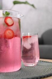 Photo of Freshly made strawberry lemonade with mint in jug and glass on wooden table indoors, closeup