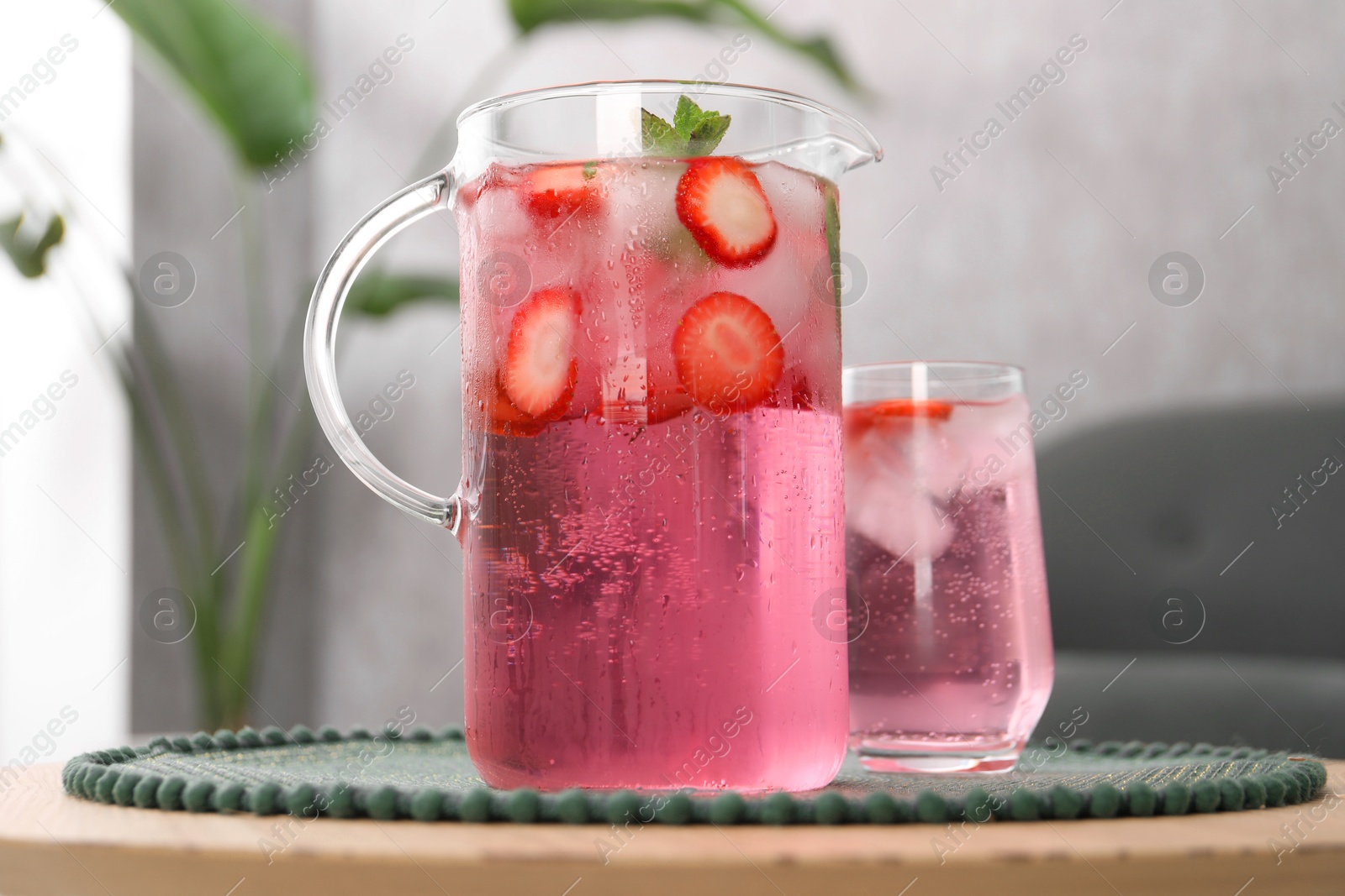 Photo of Freshly made strawberry lemonade with mint in jug and glass on wooden table indoors