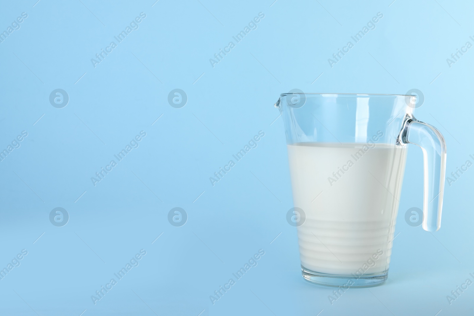 Photo of Jug of fresh milk on light blue background, space for text