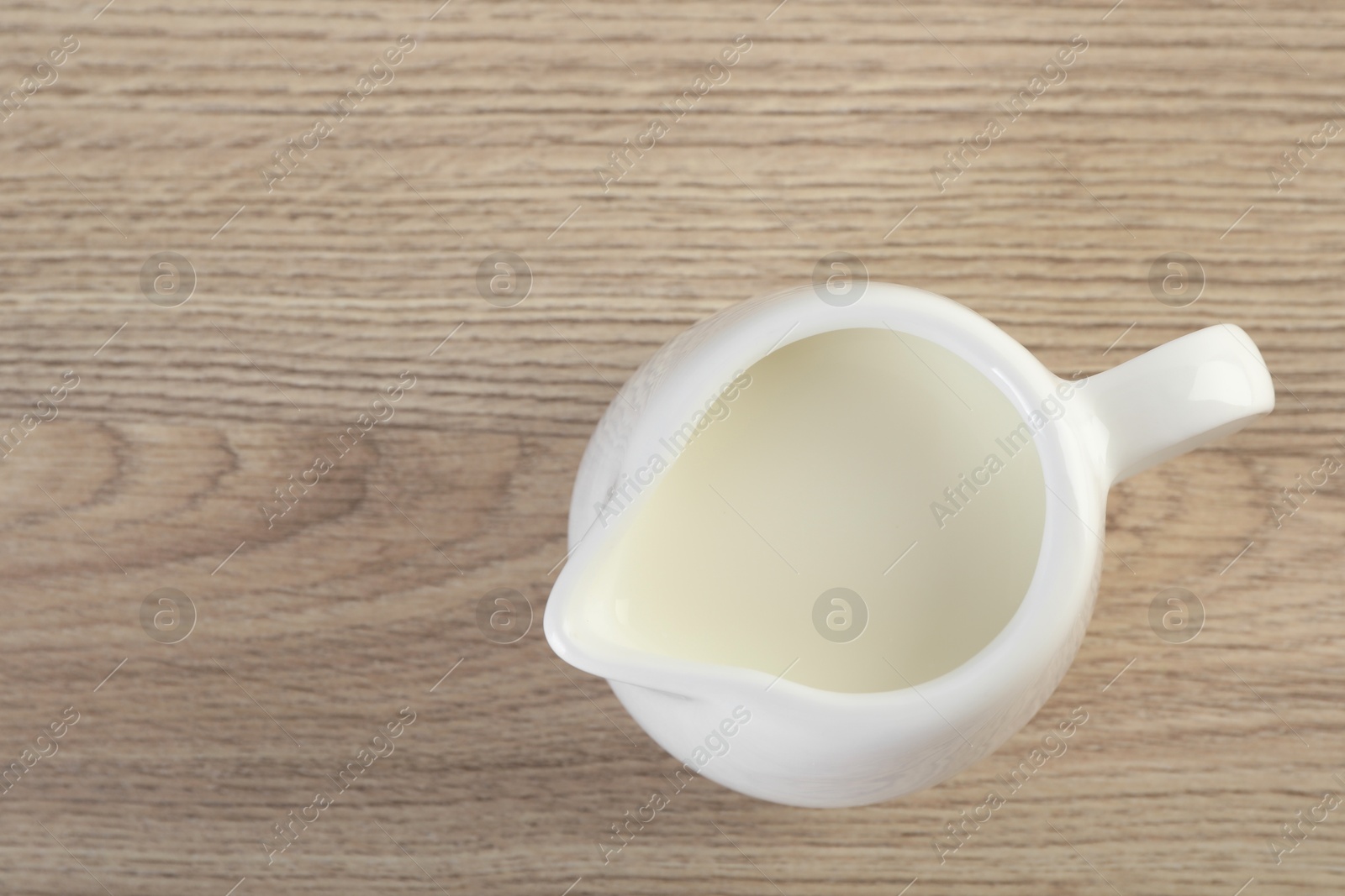 Photo of Jug of fresh milk isolated on wooden table, top view. Space for text