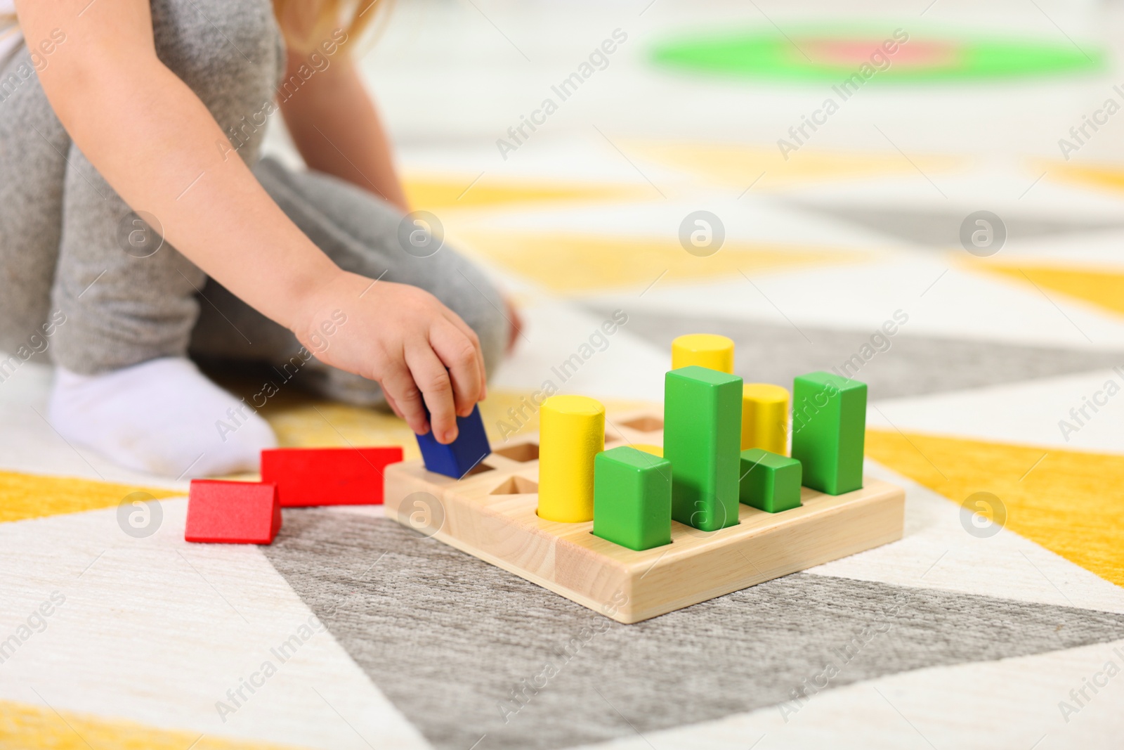 Photo of Little girl playing with set of wooden geometric figures on carpet, closeup. Kindergarten activities for motor skills development