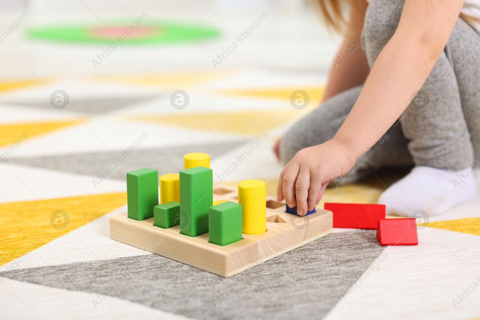 Photo of Little girl playing with set of wooden geometric figures on carpet, closeup. Kindergarten activities for motor skills development