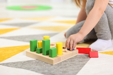 Photo of Little girl playing with set of wooden geometric figures on carpet, closeup. Kindergarten activities for motor skills development