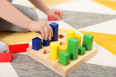 Photo of Little girl playing with set of wooden geometric figures on carpet, closeup. Kindergarten activities for motor skills development