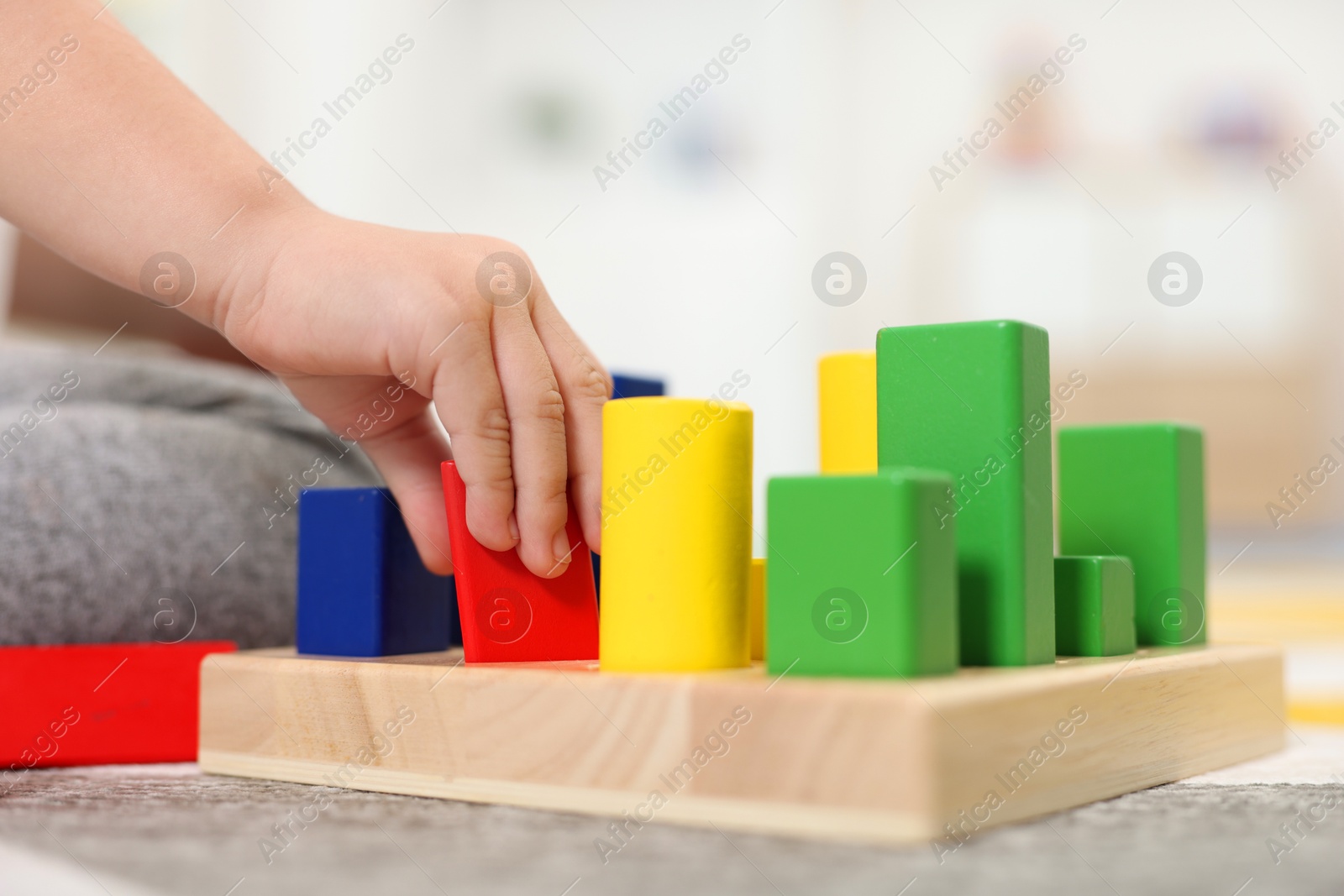 Photo of Little girl playing with set of wooden geometric figures on carpet, closeup. Kindergarten activities for motor skills development