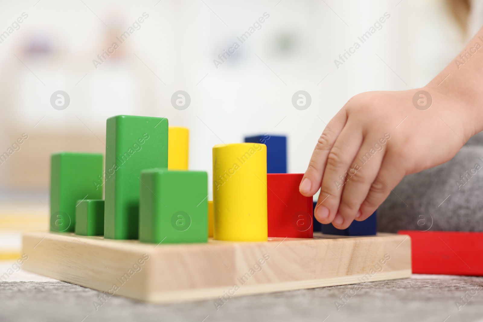 Photo of Little girl playing with set of wooden geometric figures on carpet, closeup. Kindergarten activities for motor skills development