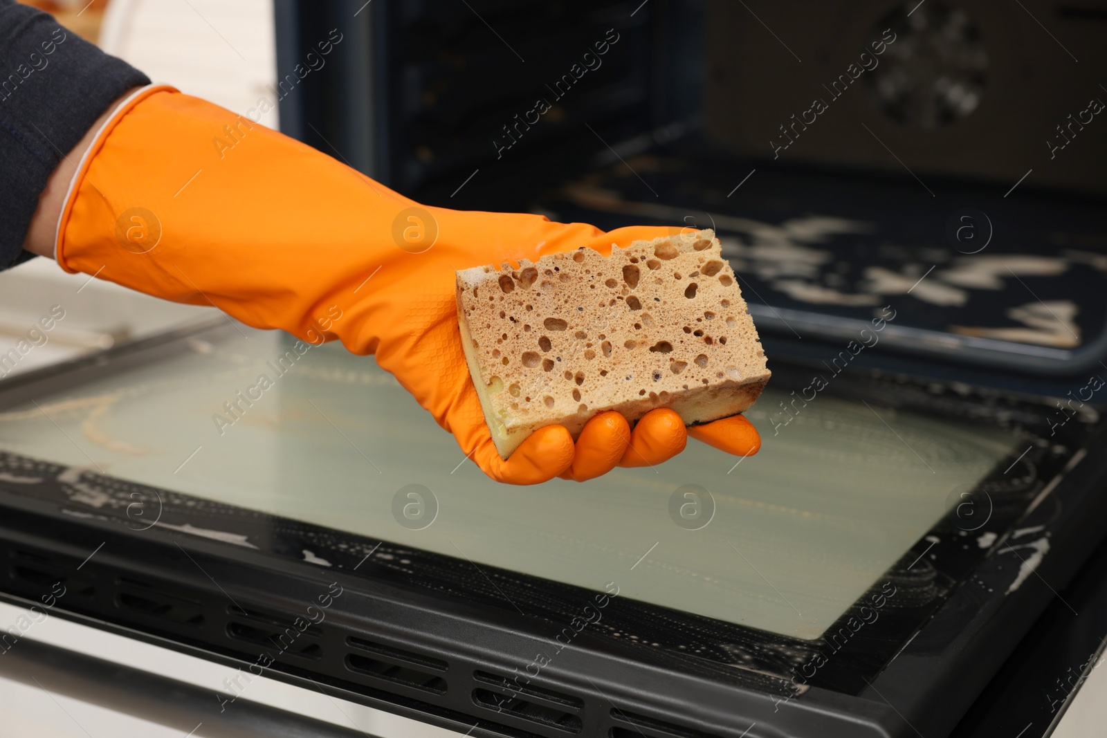 Photo of Woman showing dirty sponge after cleaning oven in kitchen, closeup