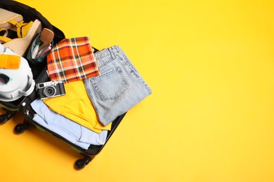 Photo of Open suitcase with traveler's belongings on yellow background, top view. Space for text