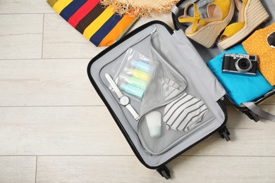 Open suitcase with traveler's belongings on floor, flat lay. Space for text