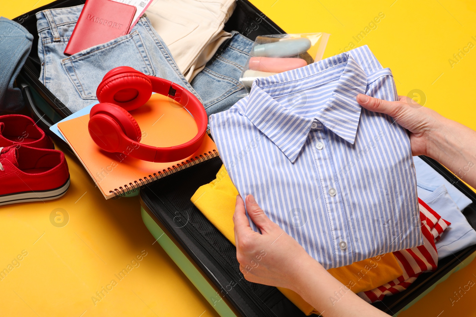 Photo of Woman packing suitcase for trip on yellow background, closeup