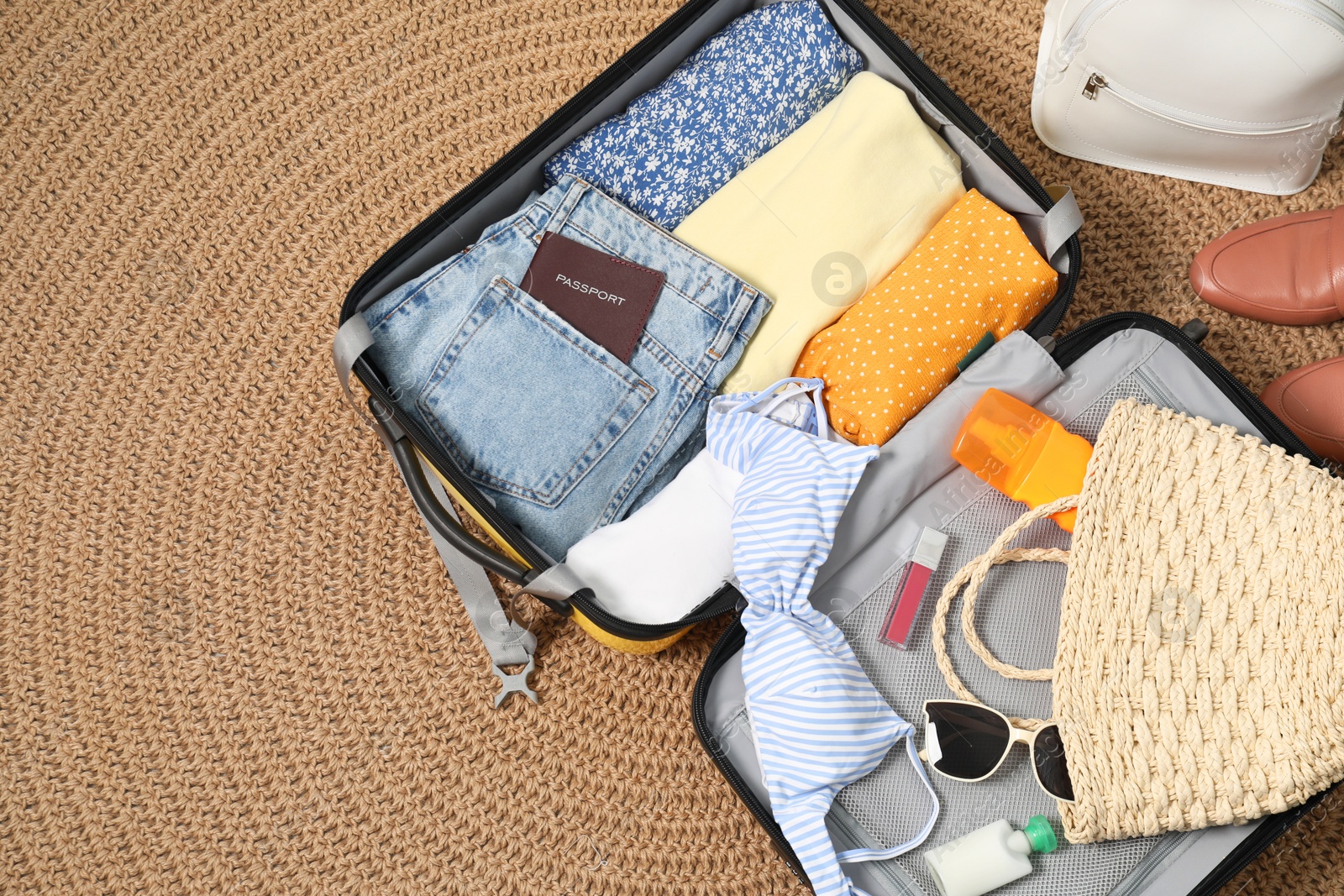 Photo of Open suitcase with traveler's belongings on rug, flat lay. Space for text