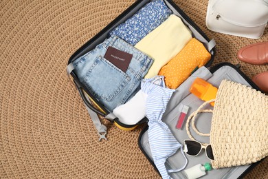 Open suitcase with traveler's belongings on rug, flat lay. Space for text