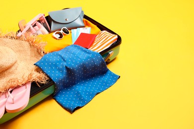 Open suitcase with traveler's belongings on yellow background, space for text