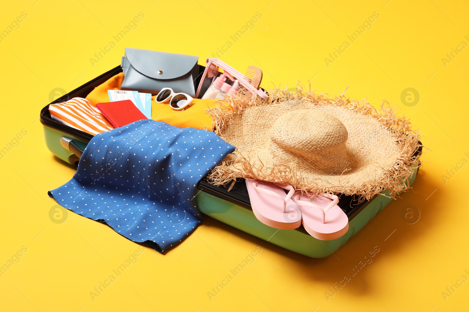 Photo of Open suitcase with traveler's belongings on yellow background