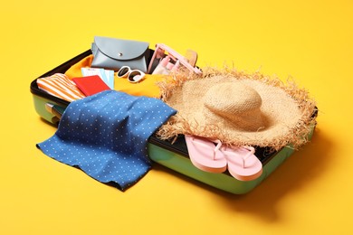 Open suitcase with traveler's belongings on yellow background