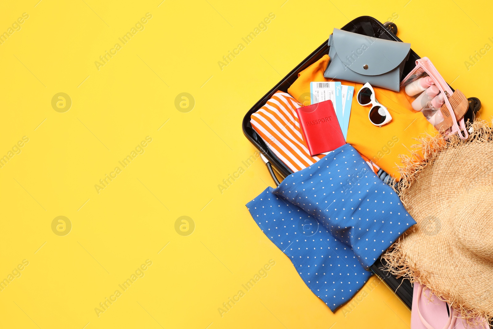 Photo of Open suitcase with traveler's belongings on yellow background, top view. Space for text