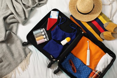 Open suitcase with traveler's belongings on bed, flat lay