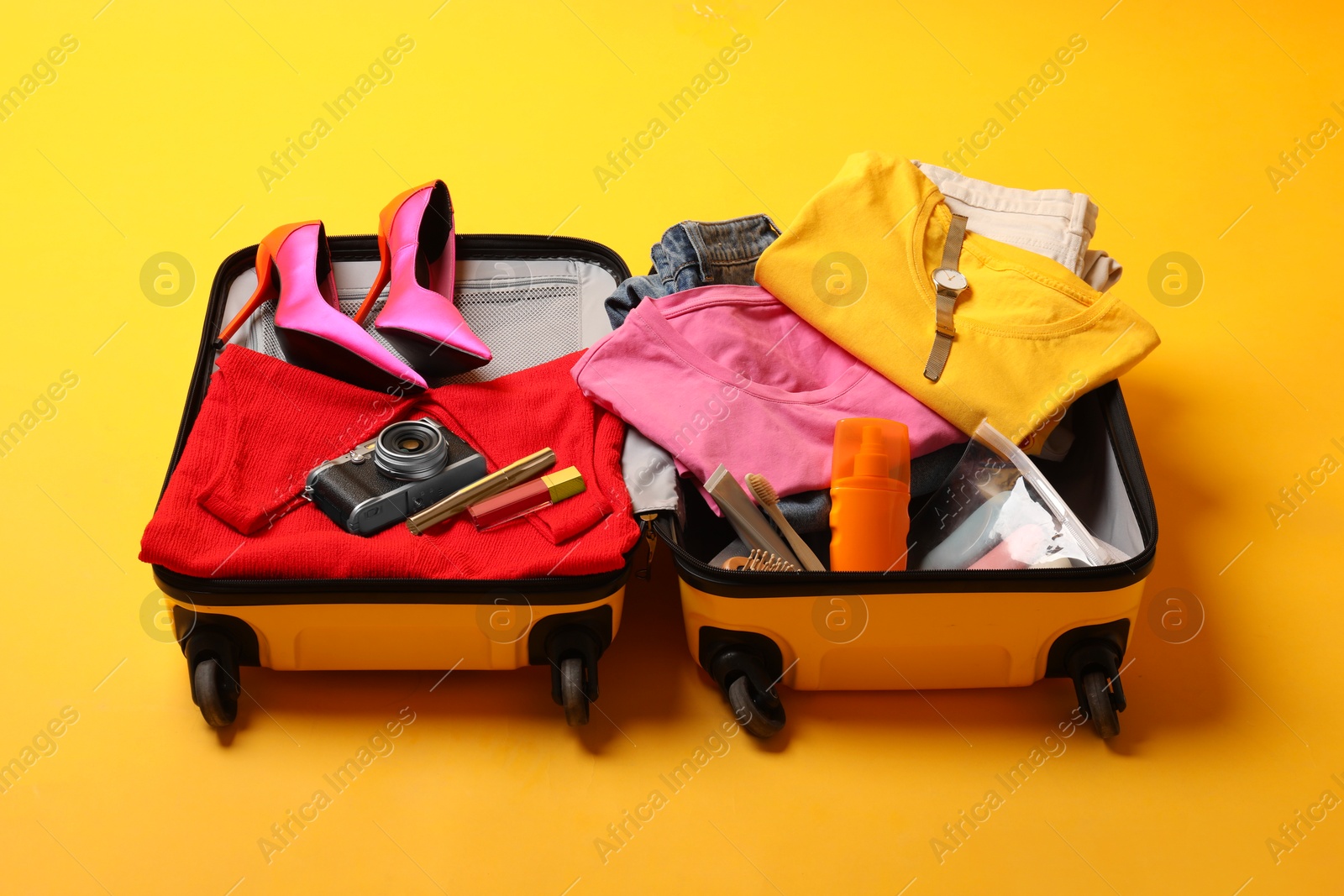 Photo of Open suitcase with traveler's belongings on yellow background