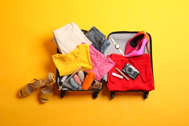 Photo of Open suitcase with traveler's belongings on yellow background, top view