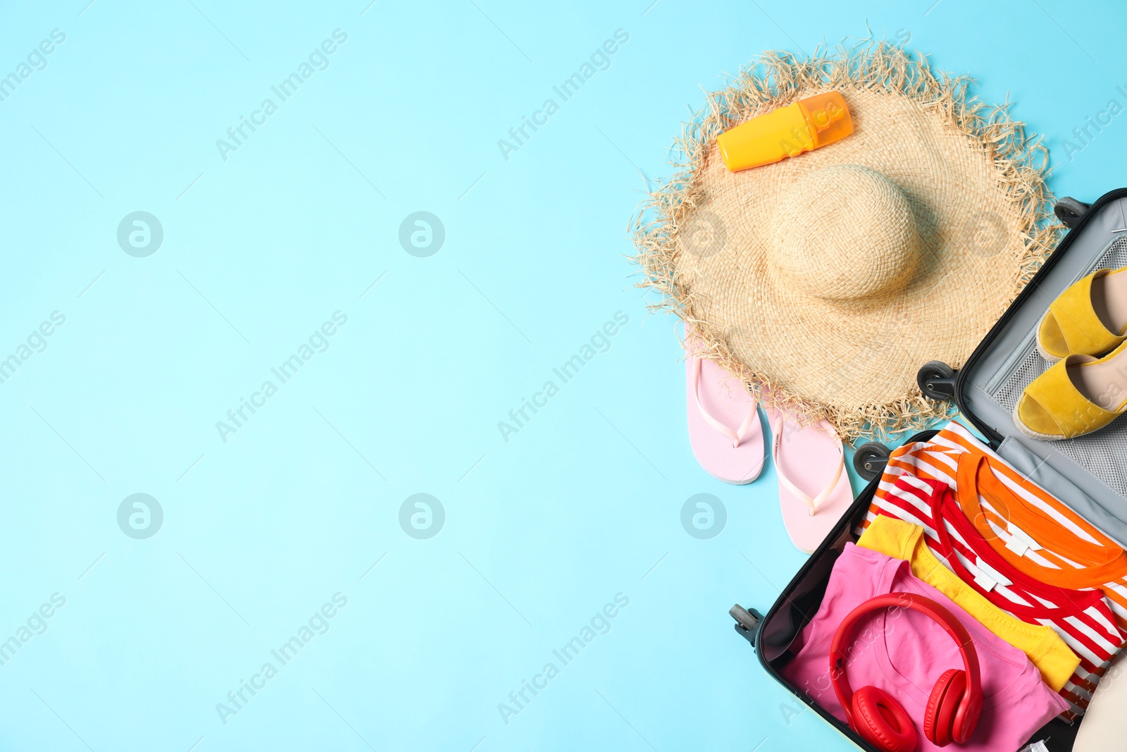 Photo of Open suitcase with traveler's belongings on light blue background, flat lay. Space for text