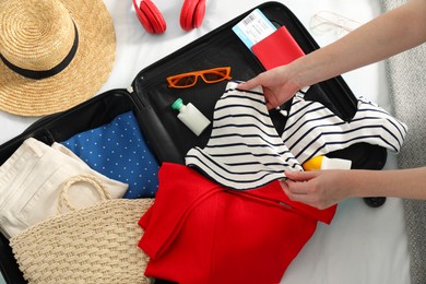 Woman packing suitcase for trip in bedroom, top view