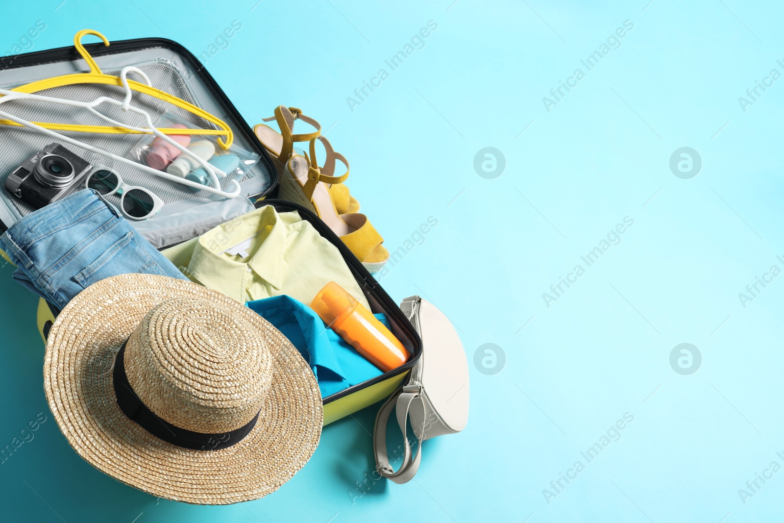 Photo of Open suitcase with traveler's belongings on light blue background, above view. Space for text