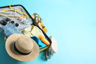 Photo of Open suitcase with traveler's belongings on light blue background, above view. Space for text