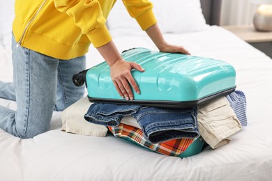 Woman packing suitcase for trip on bed indoors, closeup