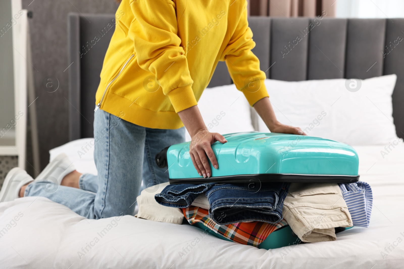 Photo of Woman packing suitcase for trip on bed indoors, closeup