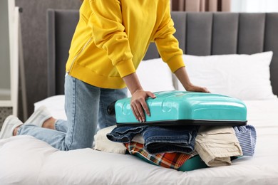 Woman packing suitcase for trip on bed indoors, closeup