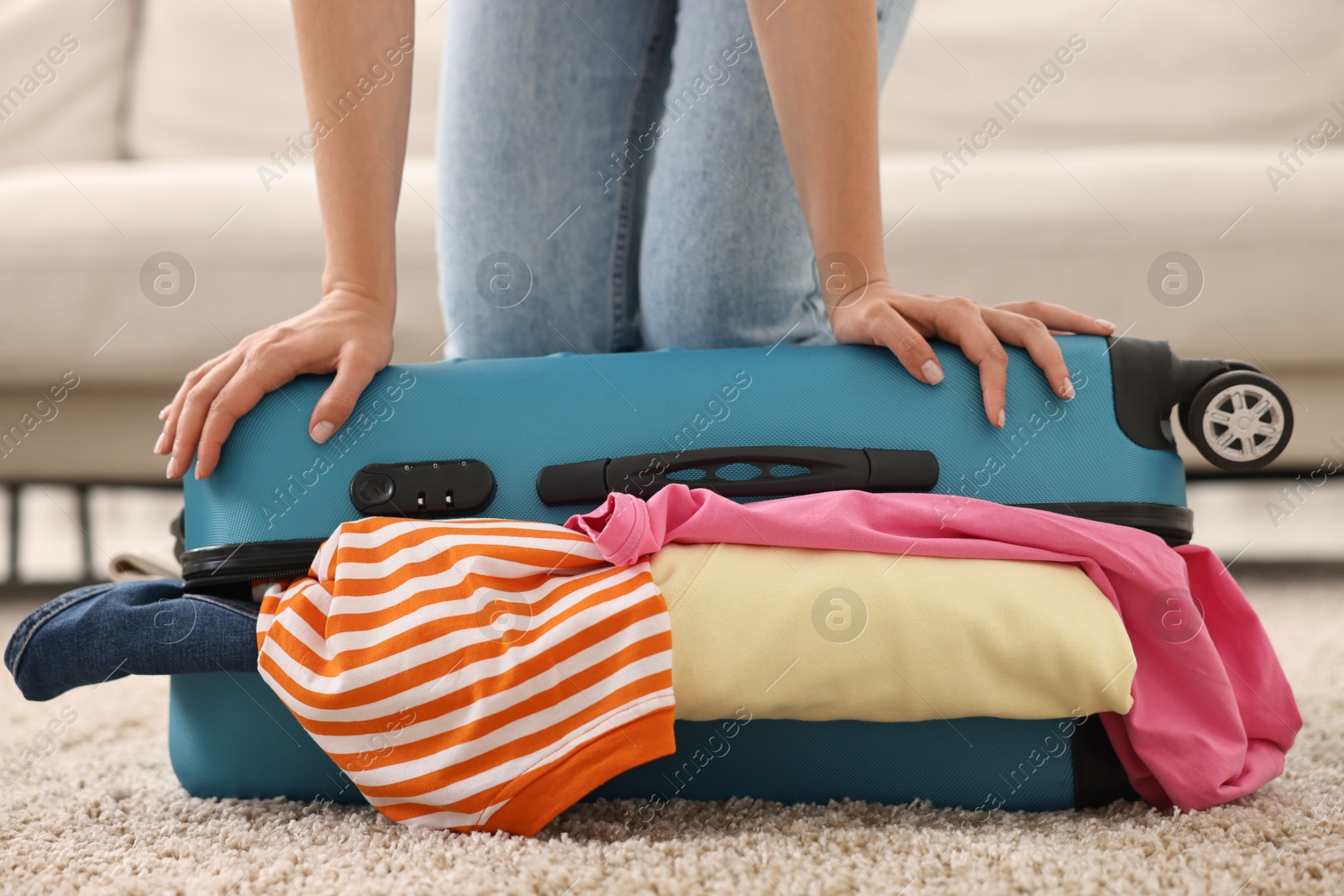 Photo of Woman packing suitcase for trip on floor indoors, closeup