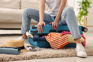 Woman packing suitcase for trip on floor indoors, closeup