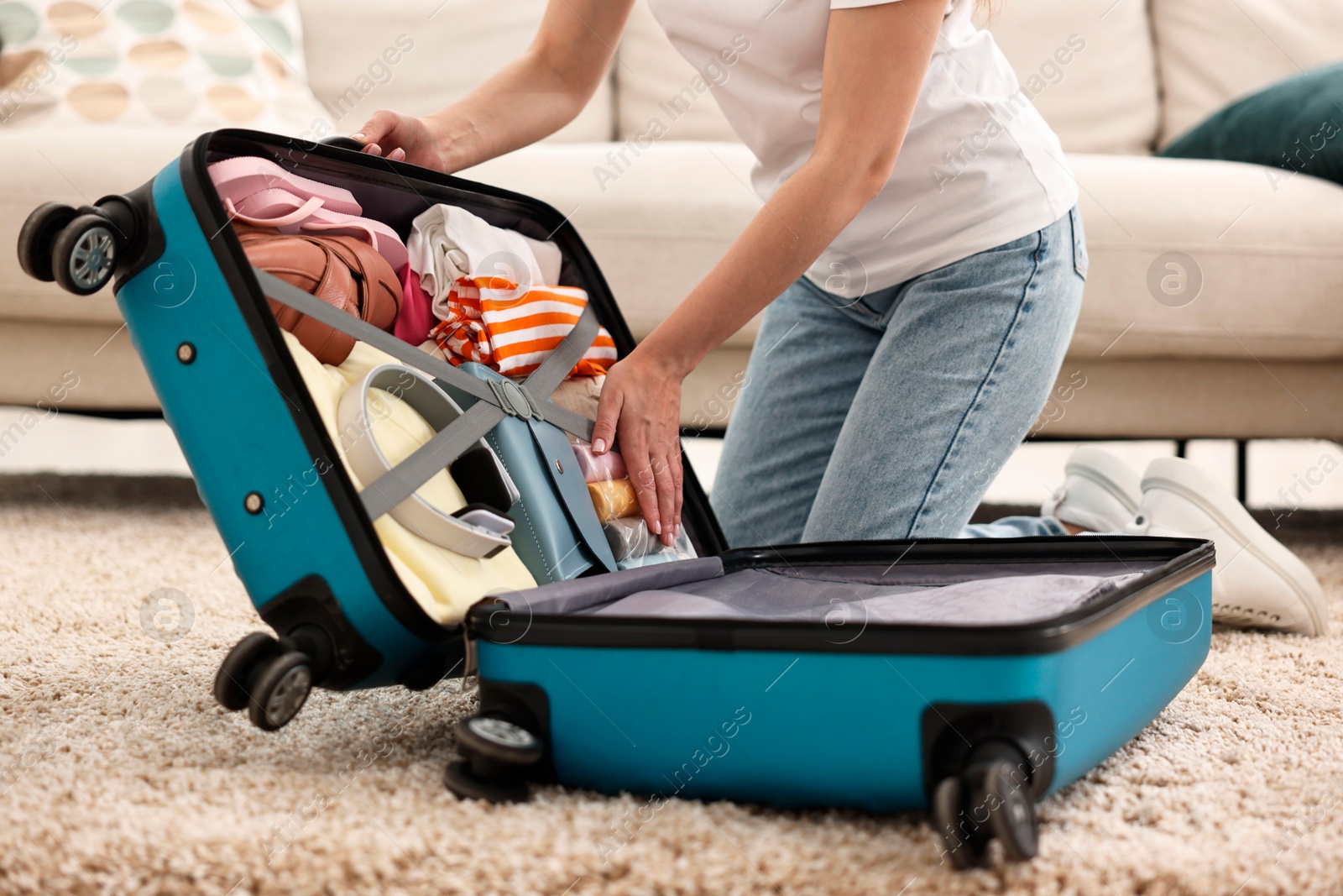 Photo of Woman packing suitcase for trip on floor indoors, closeup