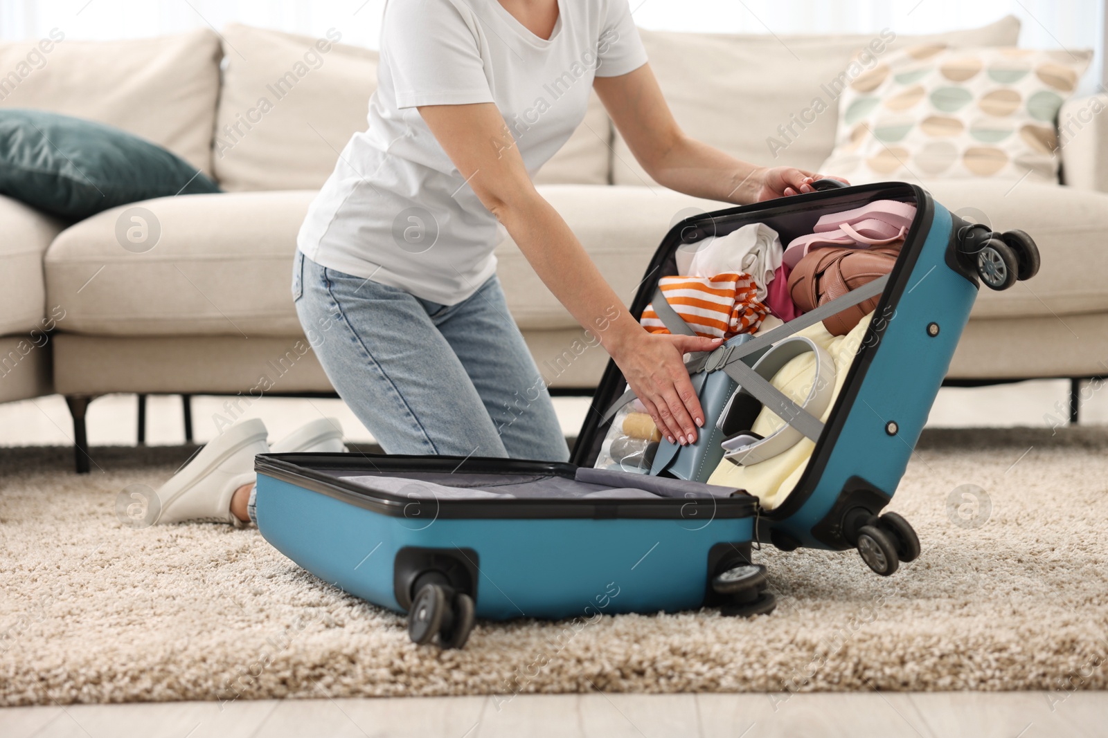 Photo of Woman packing suitcase for trip on floor indoors, closeup