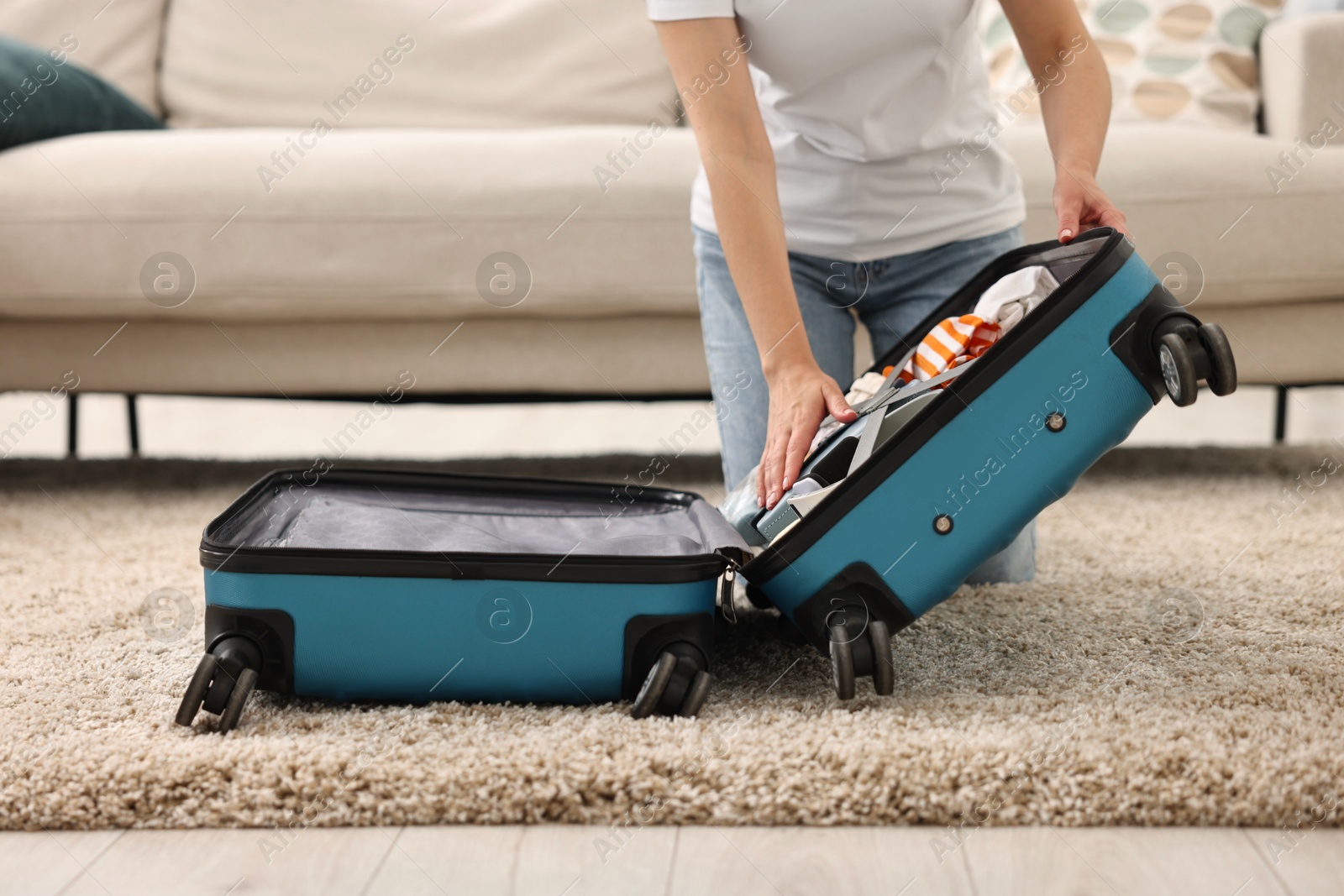 Photo of Woman packing suitcase for trip on floor indoors, closeup