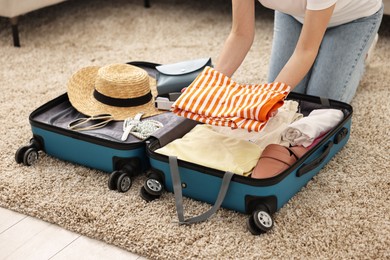 Woman packing suitcase for trip on floor indoors, closeup