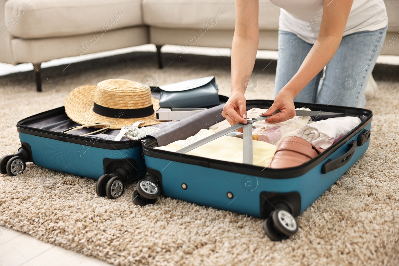 Photo of Woman packing suitcase for trip on floor indoors, closeup