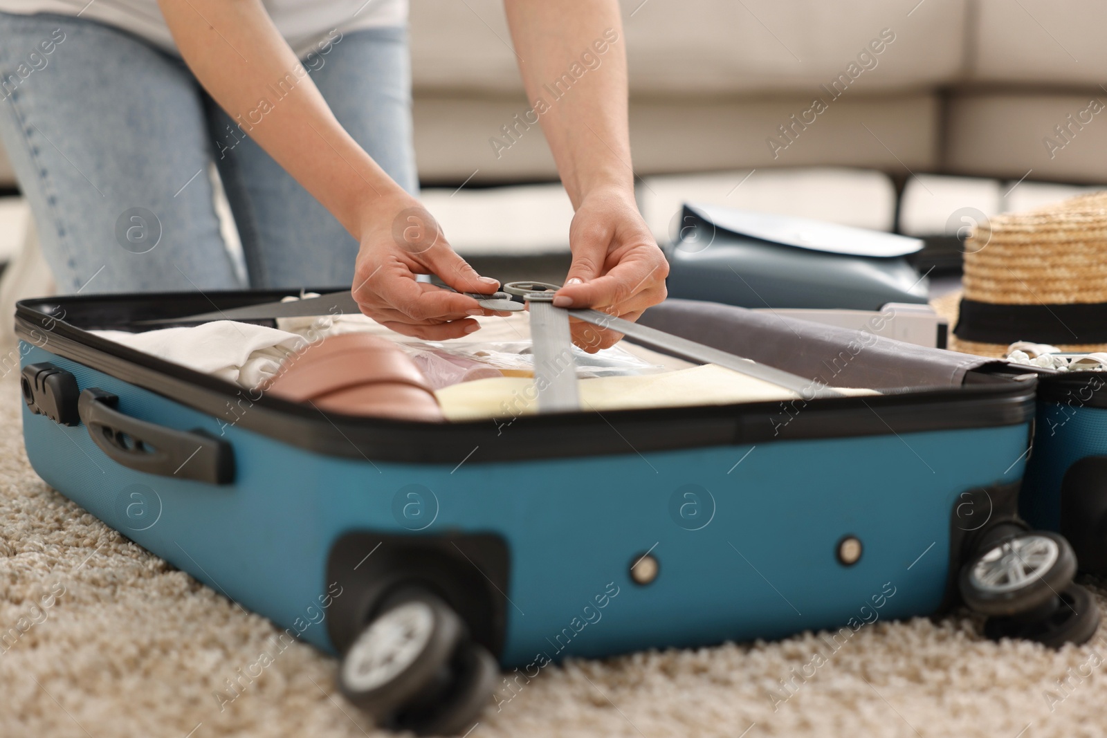 Photo of Woman packing suitcase for trip on floor indoors, closeup