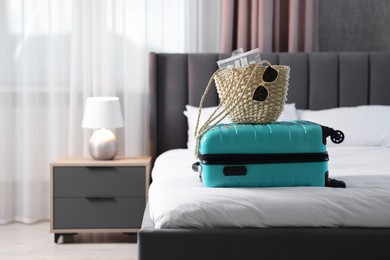 Photo of Turquoise suitcase, bag, sunglasses and cosmetic travel kit on bed indoors