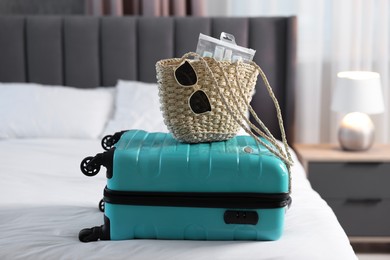 Turquoise suitcase, bag, sunglasses and cosmetic travel kit on bed indoors