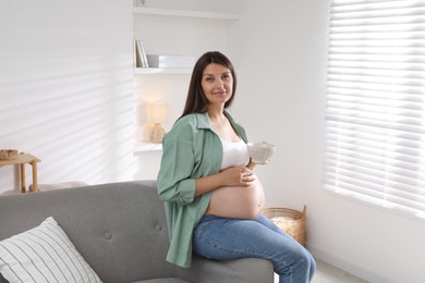 Beautiful pregnant woman sitting on sofa at home