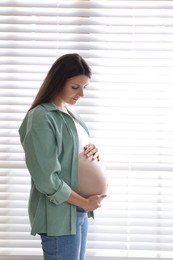 Beautiful pregnant woman near window blinds at home