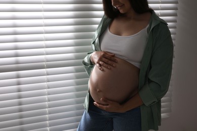 Photo of Beautiful pregnant woman near window blinds at home, closeup. Space for text