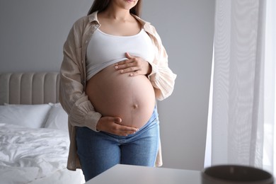 Photo of Pregnant woman in beige shirt at home, closeup