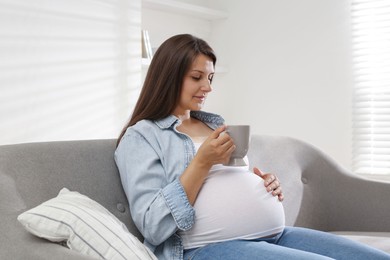 Photo of Beautiful pregnant woman with cup on sofa at home