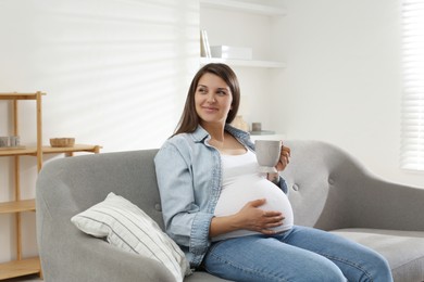 Photo of Beautiful pregnant woman with cup on sofa at home