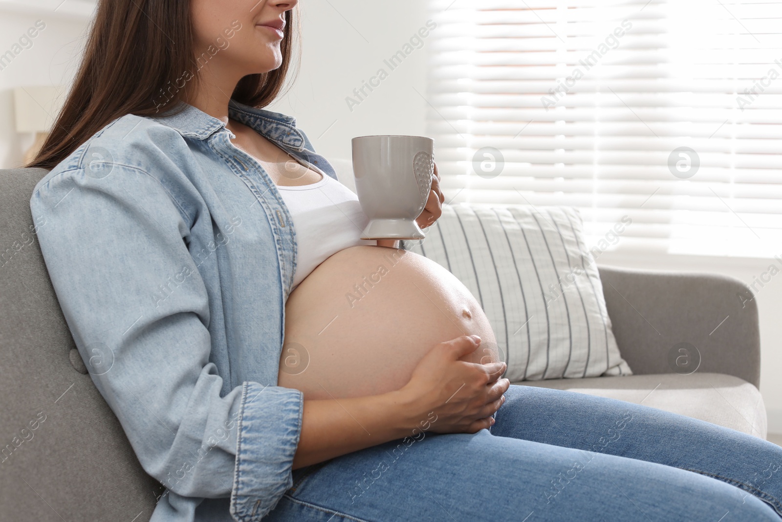 Photo of Pregnant woman with cup on sofa at home, closeup