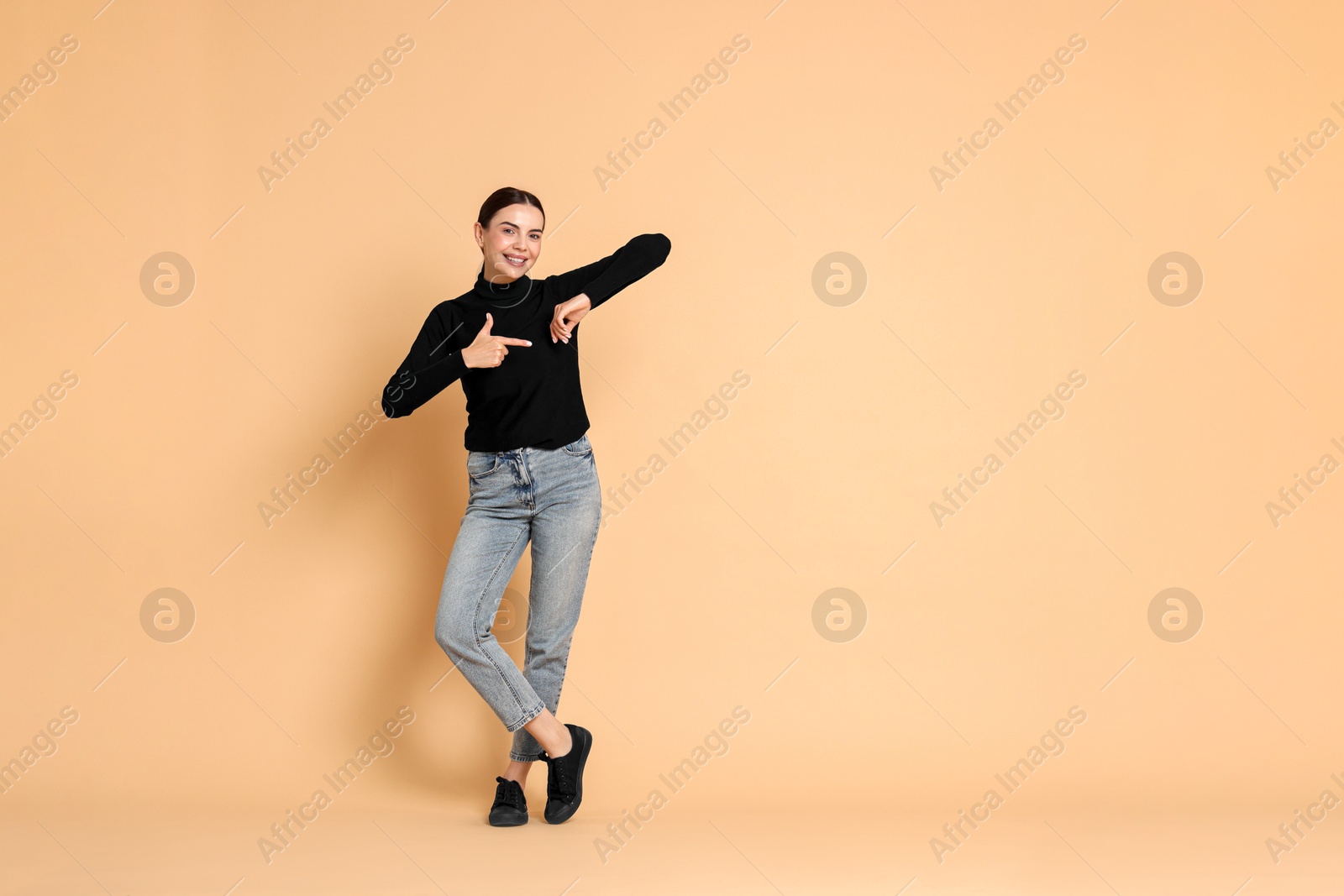 Photo of Smiling woman pointing at something on beige background. Space for text